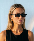 Model wearing Maelle slim rectangular sunglasses in black with gray lenses
